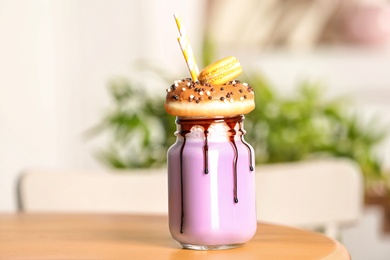 Photo of Mason jar with delicious milk shake on table against blurred background