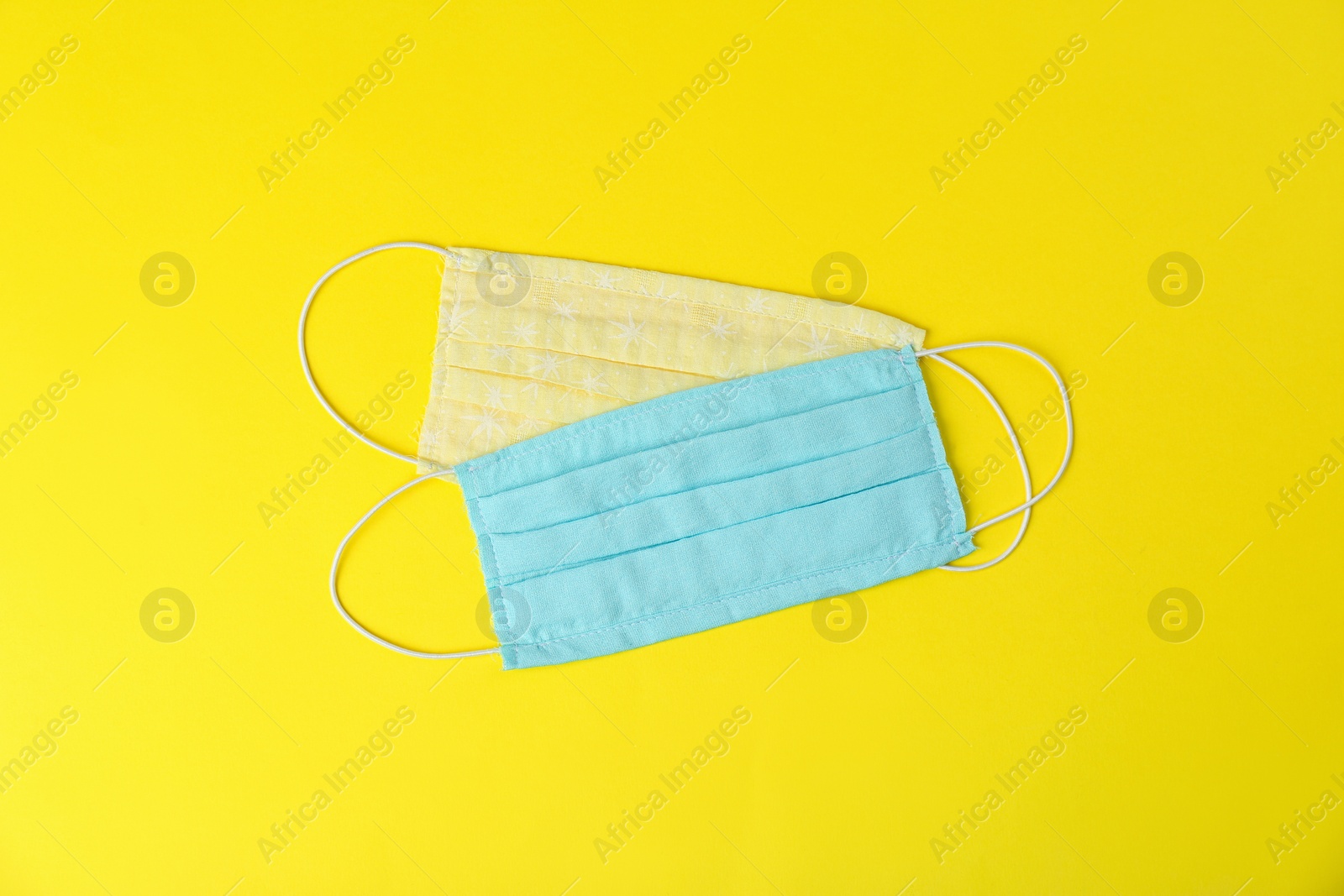 Photo of Homemade protective face masks on yellow background, flat lay