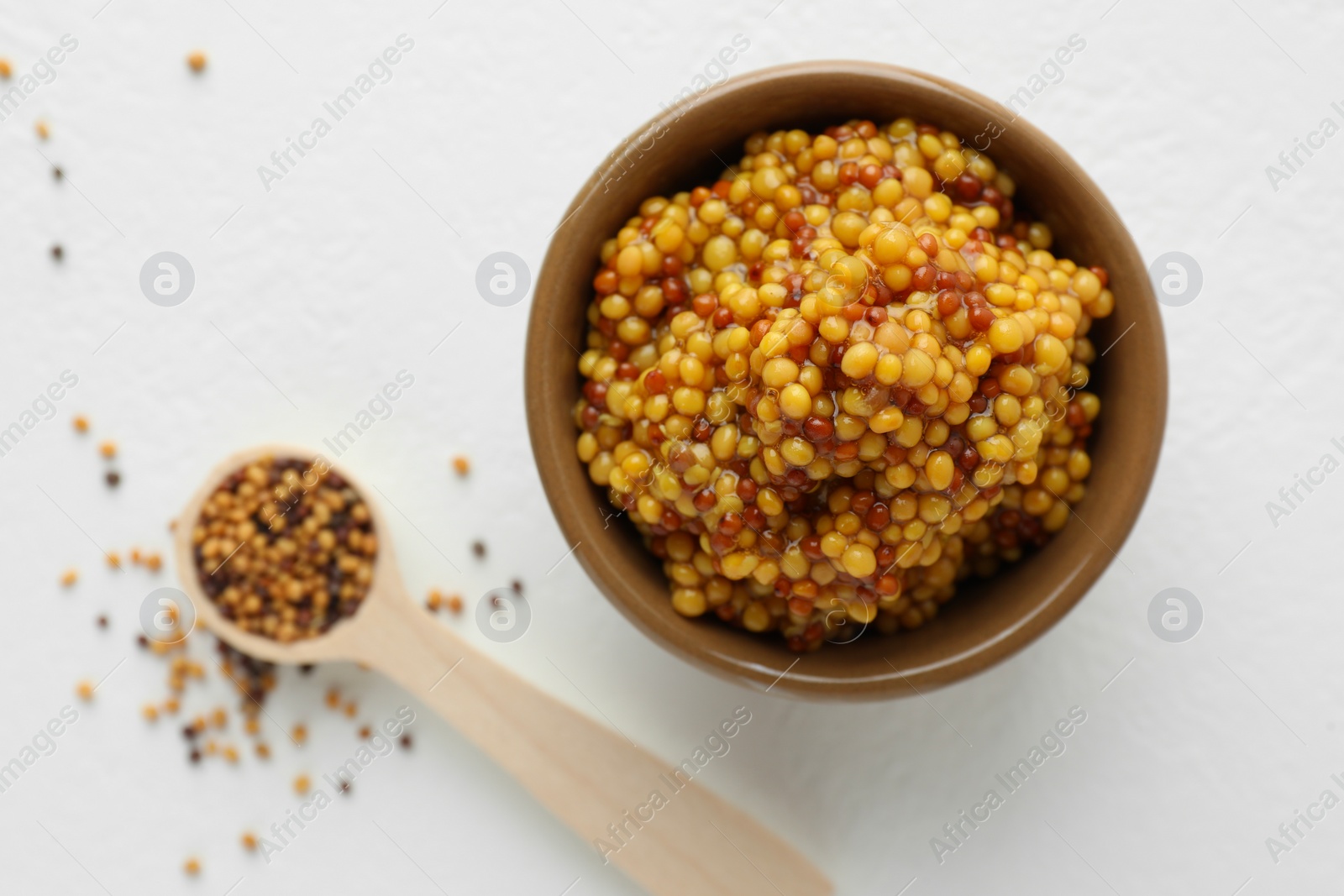 Photo of Fresh whole grain mustard in bowl and dry seeds on white table, flat lay