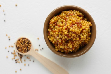 Fresh whole grain mustard in bowl and dry seeds on white table, flat lay