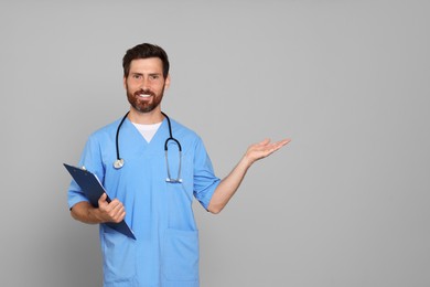 Happy doctor with stethoscope and clipboard on light grey background. Space for text
