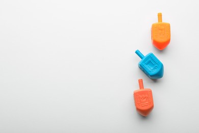 Photo of Colorful dreidels on white background, flat lay with space for text. Traditional Hanukkah game