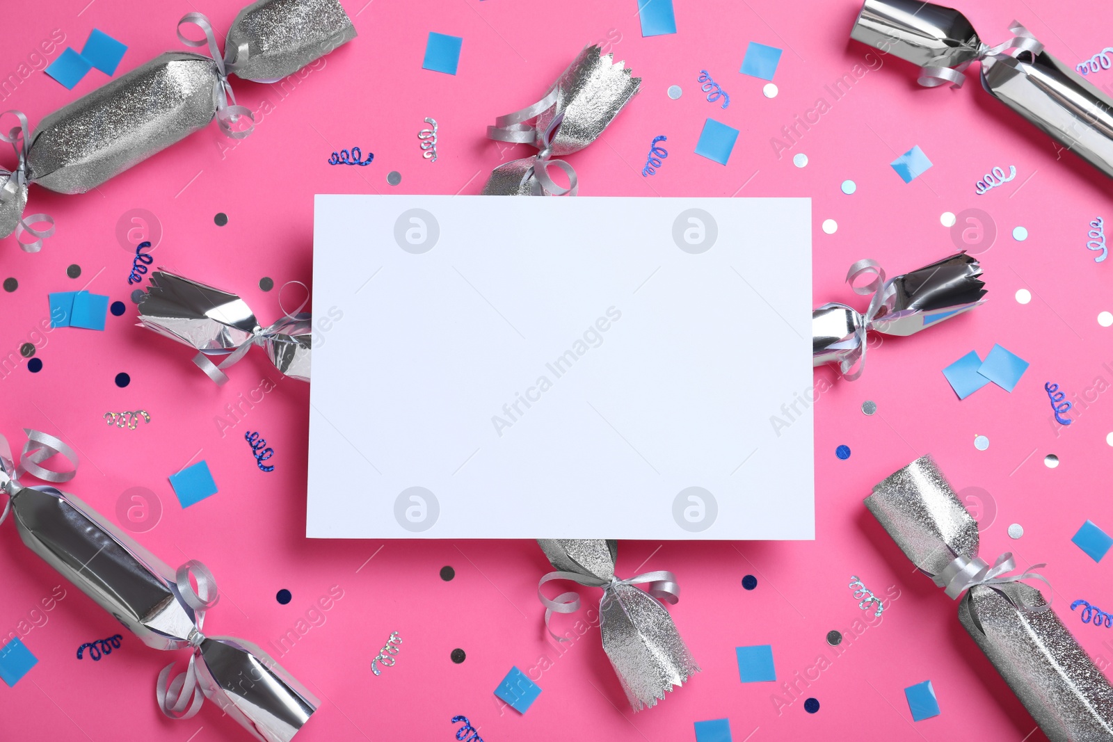 Photo of Flat lay composition of silver Christmas crackers with shiny confetti and blank card on pink background. Space for text
