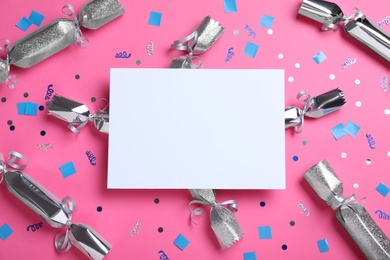 Flat lay composition of silver Christmas crackers with shiny confetti and blank card on pink background. Space for text