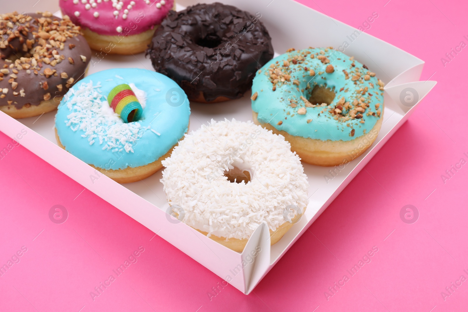 Photo of Box with different tasty glazed donuts on pink background, closeup