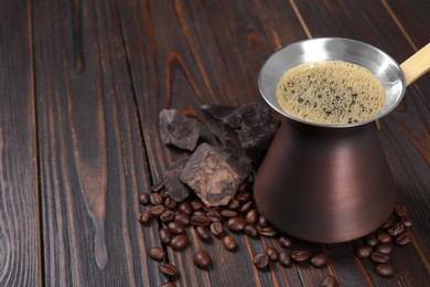 Photo of Hot turkish coffee pot, beans and chocolate on wooden table, space for text