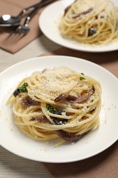 Plates of delicious pasta with anchovies, olives and parmesan cheese served on light wooden table