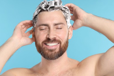 Photo of Happy man washing his hair with shampoo on light blue background, closeup