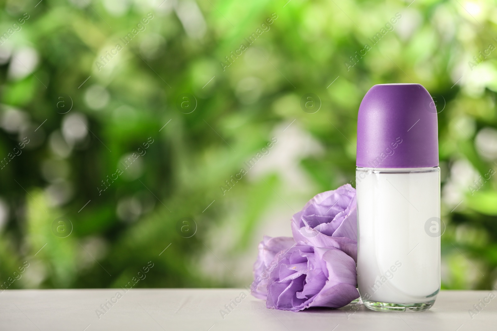 Photo of Deodorant container and Eustoma flowers on white wooden table against blurred background. Space for text