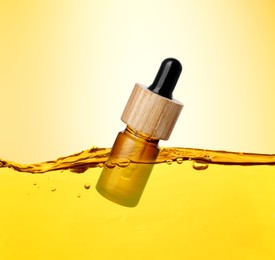 Image of Bottle of cosmetic product floating in essential oil against gold gradient background