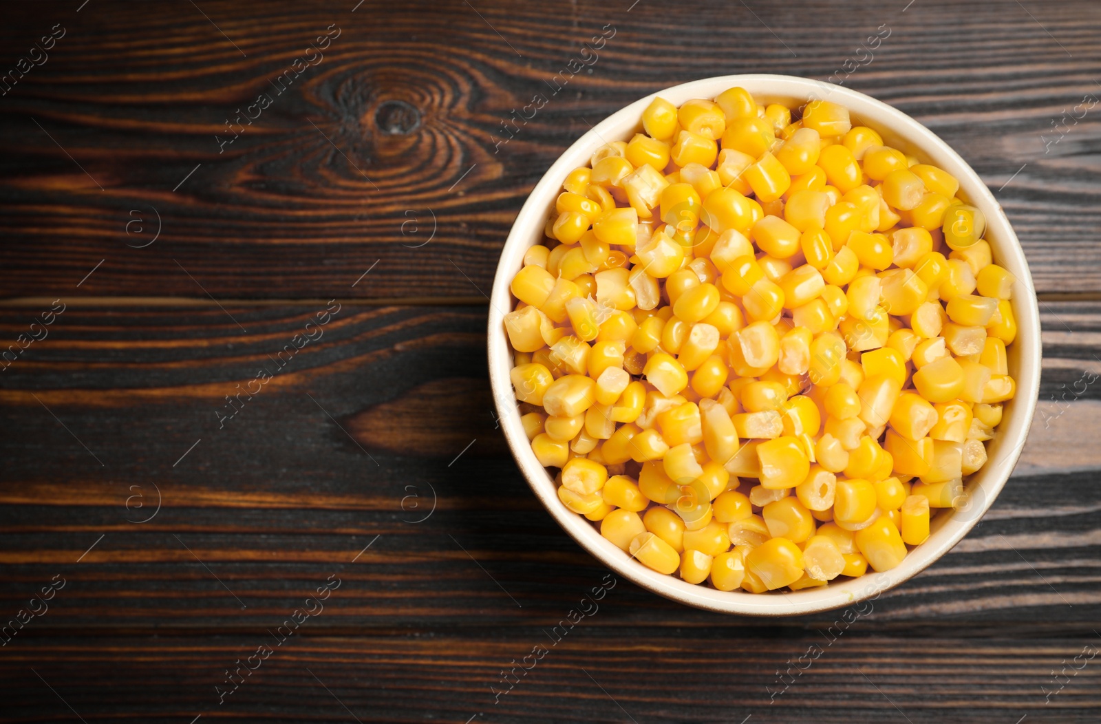 Photo of Delicious canned corn in bowl on wooden table, top view. Space for text