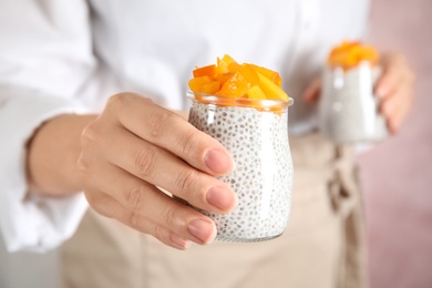 Photo of Young woman holding jars of tasty chia seed pudding with persimmon, closeup