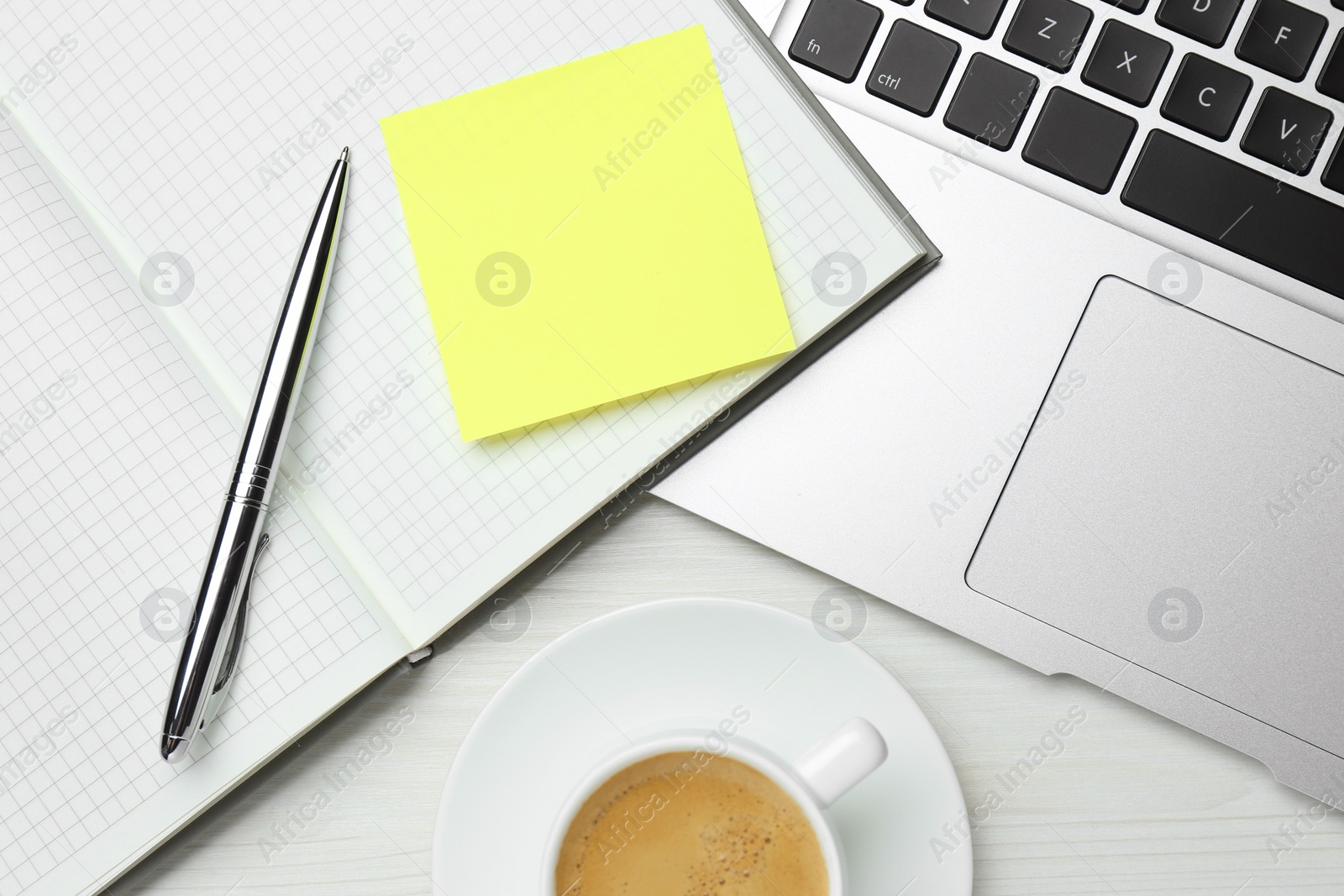 Photo of Laptop, notebook with blank sticky note, pen and cup of coffee on white wooden table, flat lay. Space for text