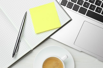 Laptop, notebook with blank sticky note, pen and cup of coffee on white wooden table, flat lay. Space for text