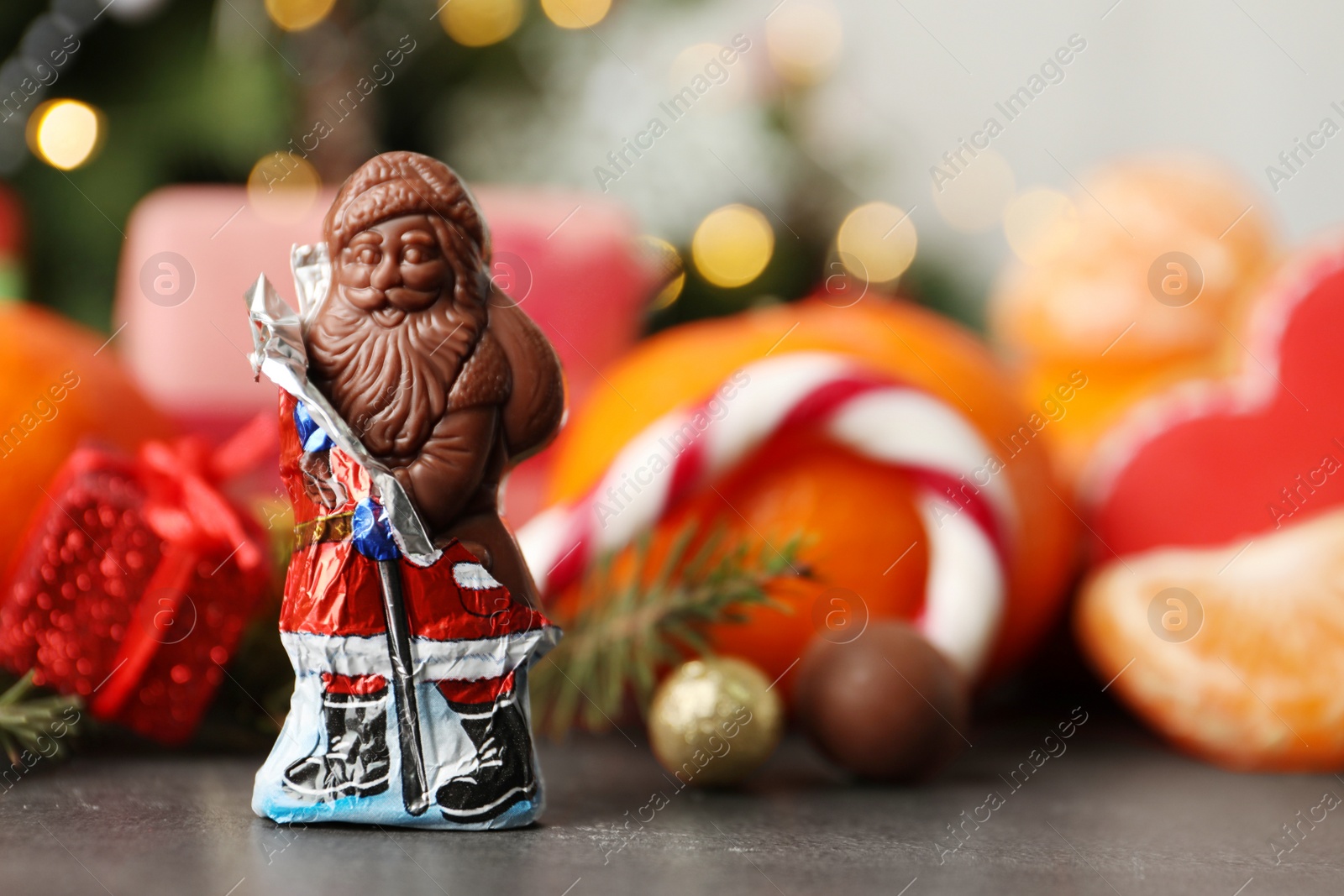 Photo of Chocolate Santa Claus candy against Christmas decorations, sweets and tangerine fruits, space for text