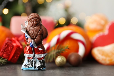 Chocolate Santa Claus candy against Christmas decorations, sweets and tangerine fruits, space for text