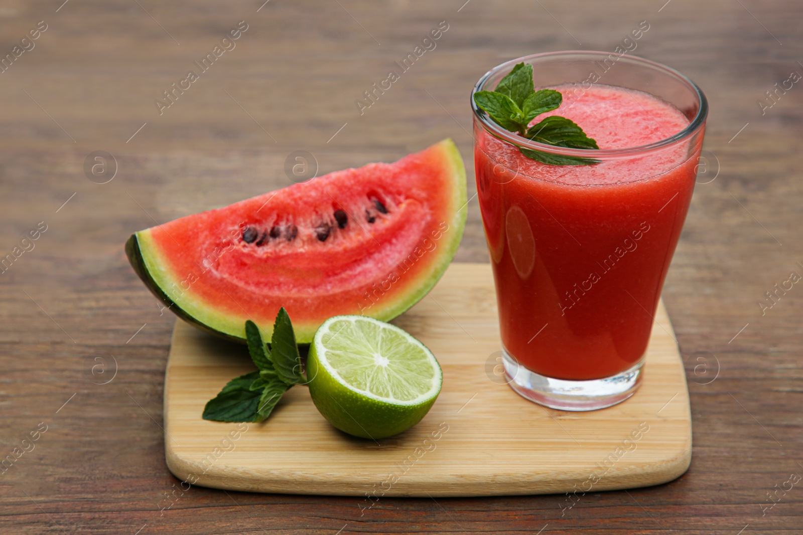 Photo of Glass of delicious watermelon smoothie with mint and fresh cut fruits on wooden table
