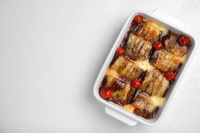 Tasty eggplant rolls with tomatoes and cheese in baking dish on white table, top view. Space for text