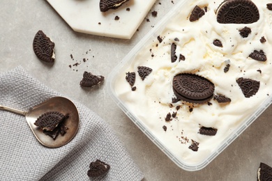 Flat lay composition with container of ice cream and chocolate cookies on grey background