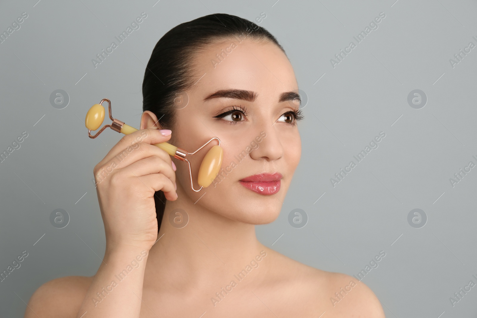 Photo of Woman using natural jade face roller on grey background