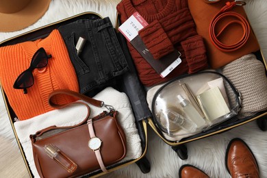 Photo of Open suitcase with folded clothes, accessories and shoes on floor, flat lay