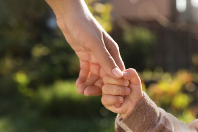 Photo of Daughter holding mother's hand outdoors, closeup view