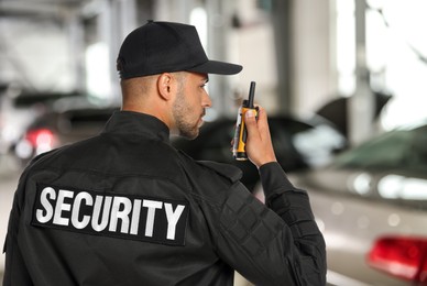 Image of Male security guard wearing uniform using portable radio transmitter at parking
