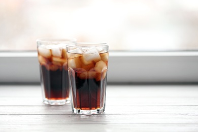 Glasses of cola with ice near window, space for text