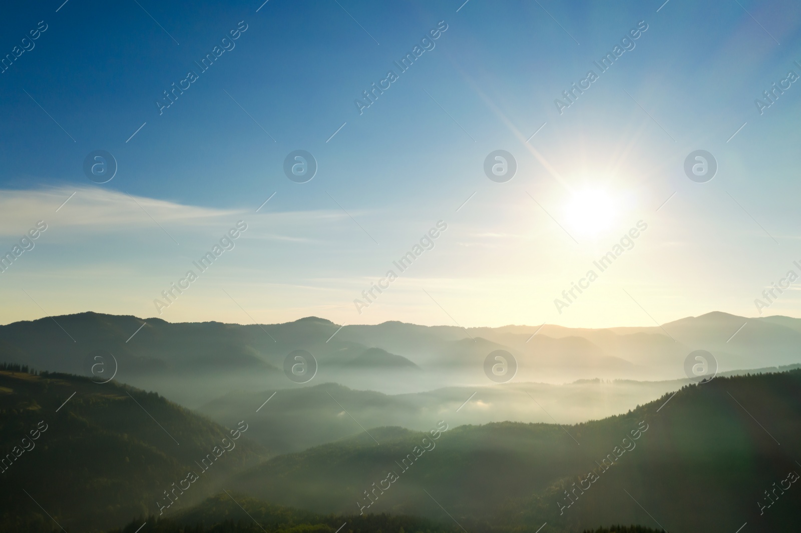 Image of Sun shining over forest in misty mountains. Drone photography