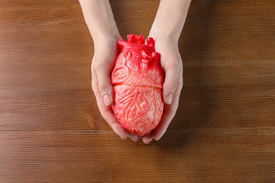 Photo of Woman holding model of heart on wooden table. Heart attack concept