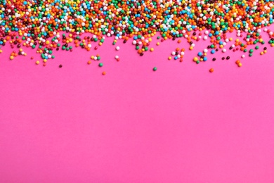 Photo of Bright colorful sprinkles on pink background, flat lay with space for text. Confectionery decor