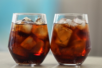 Photo of Glasses of cola with ice on table against blurred background