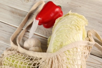 Photo of Fresh Chinese cabbage, bell pepper and garlic in net bag on wooden table, closeup