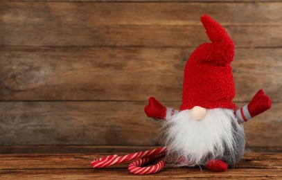 Photo of Cute Christmas gnome with candy canes on table against wooden background. Space for text