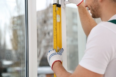 Photo of Construction worker using bubble level while installing window indoors, closeup