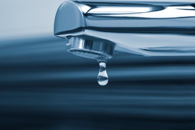 Image of Water drop falling down from tap in bathroom, closeup