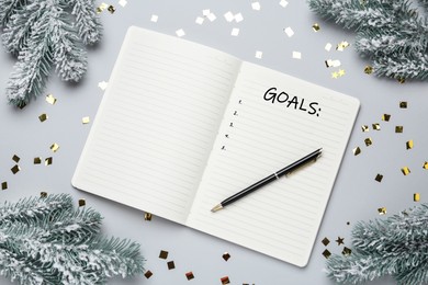 Image of Word Goals written in notebook and Christmas decor on light grey background, flat lay