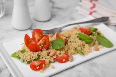 Delicious quinoa salad with tomatoes, beans and spinach leaves served on white marble table
