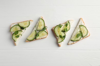 Photo of Tasty cucumber sandwiches with sesame seeds and microgreens on white wooden table, flat lay