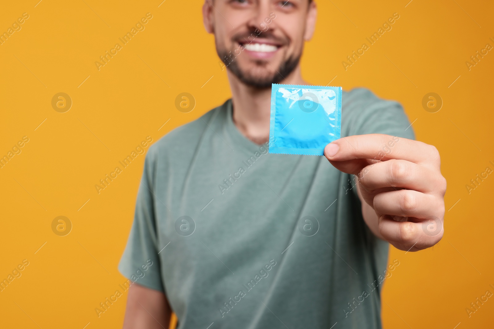 Photo of Happy man holding condom against orange background, focus on hand