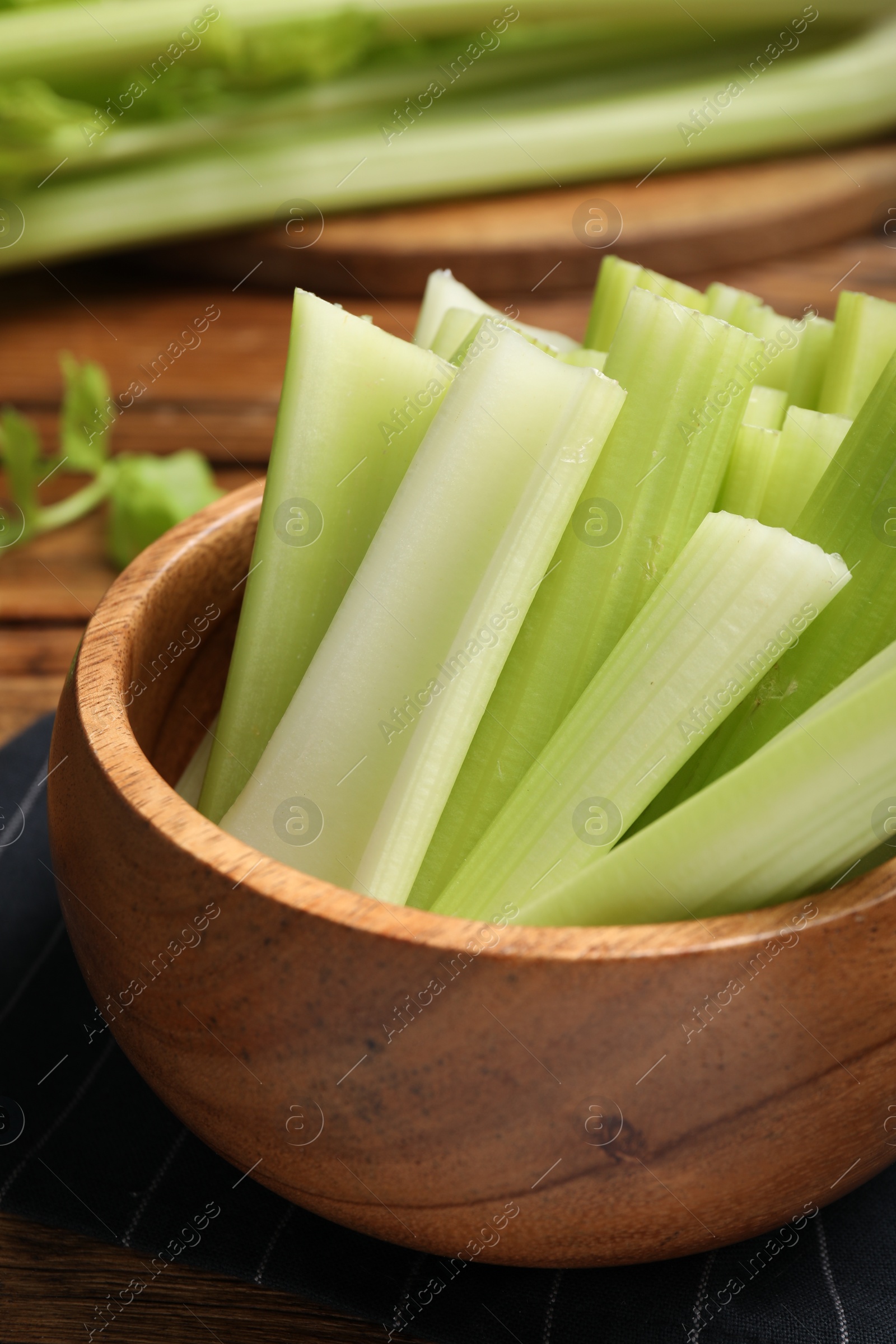 Photo of Wooden bowl of fresh cut celery on table, closeup