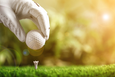 Image of Player putting golf ball on tee in sunny summer park, closeup. Space for design