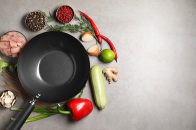 Photo of Empty iron wok surrounded by raw ingredients on grey table, flat lay. Space for text