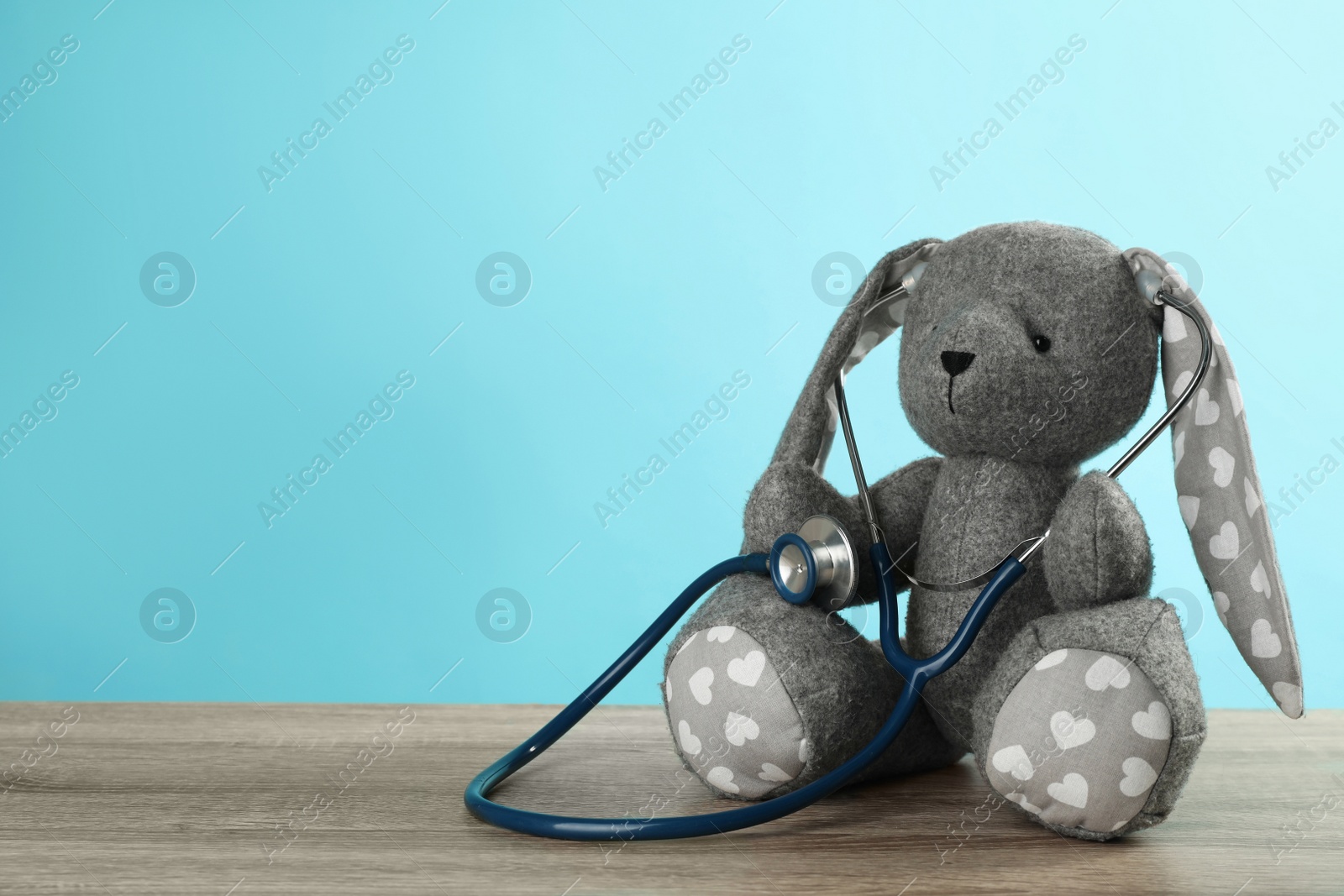 Photo of Toy bunny with stethoscope on wooden table, space for text. Pediatrician practice