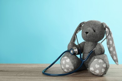 Photo of Toy bunny with stethoscope on wooden table, space for text. Pediatrician practice