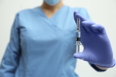 Doctor holding syringe with COVID-19 vaccine on light background, closeup