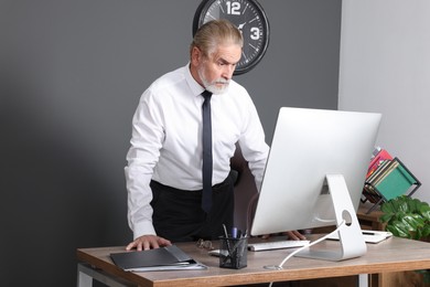 Serious senior boss working on computer at wooden table in modern office