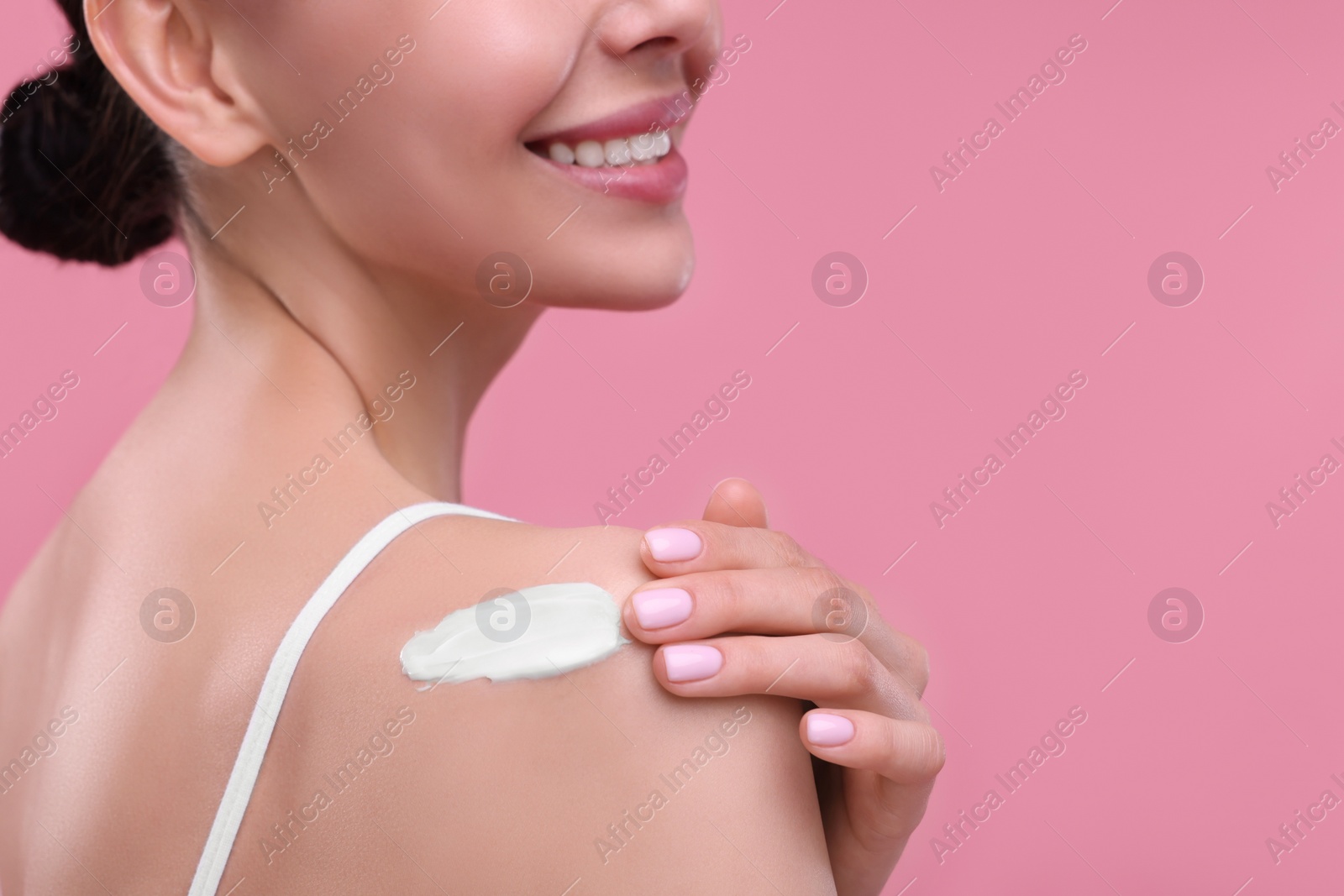 Photo of Woman with smear of body cream on her shoulder against pink background, closeup. Space for text