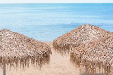 Photo of Beautiful straw umbrellas on sandy beach near sea