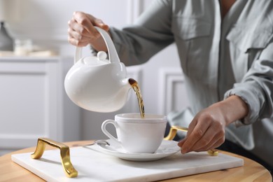 Photo of Woman pouring hot tea into cup at wooden table, closeup